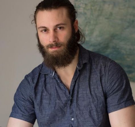 Un hombre con barba y cabello largo recogido, con una camisa azul